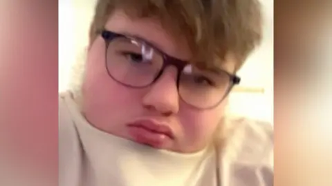 Supplied A boy with mousey hair wears a cream top and dark-rimmed spectacles while looking at the camera.