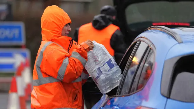 A woman in hi-vis passes water through a window