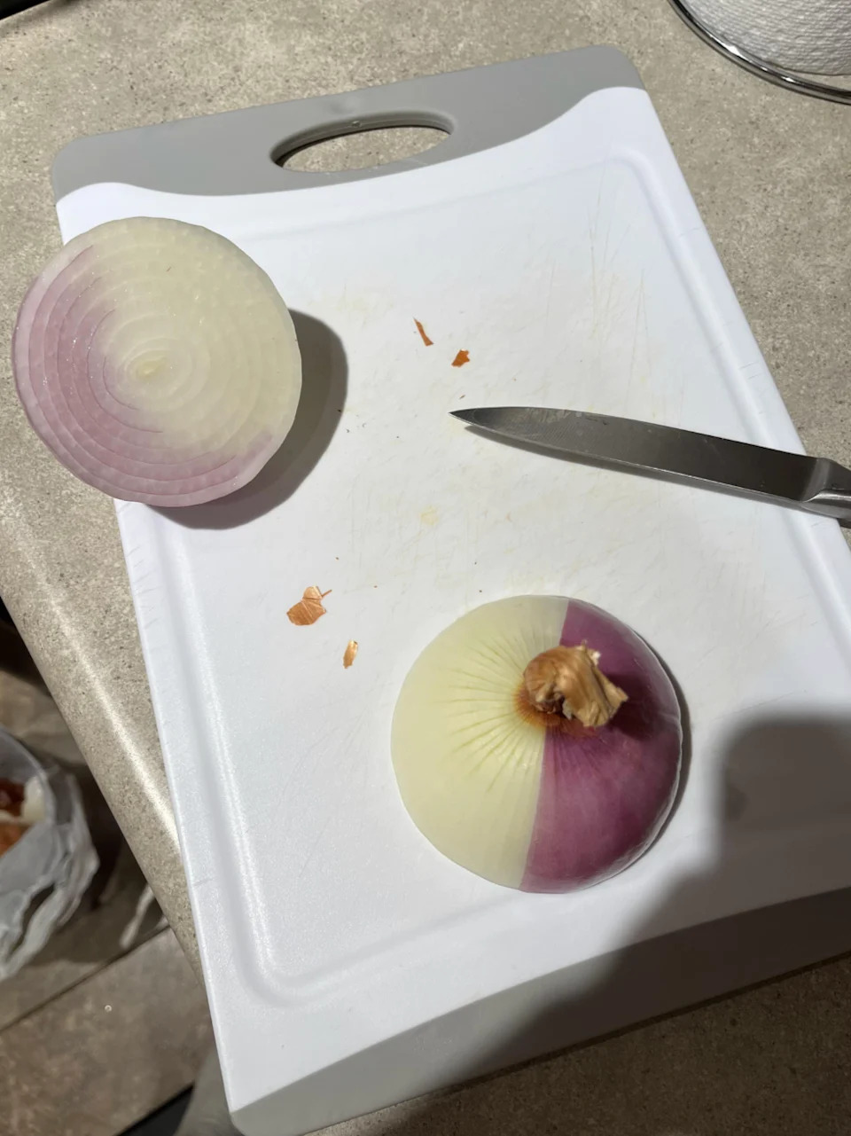 Half-sliced onion with a section showing purple and white layers on a cutting board, accompanied by a knife