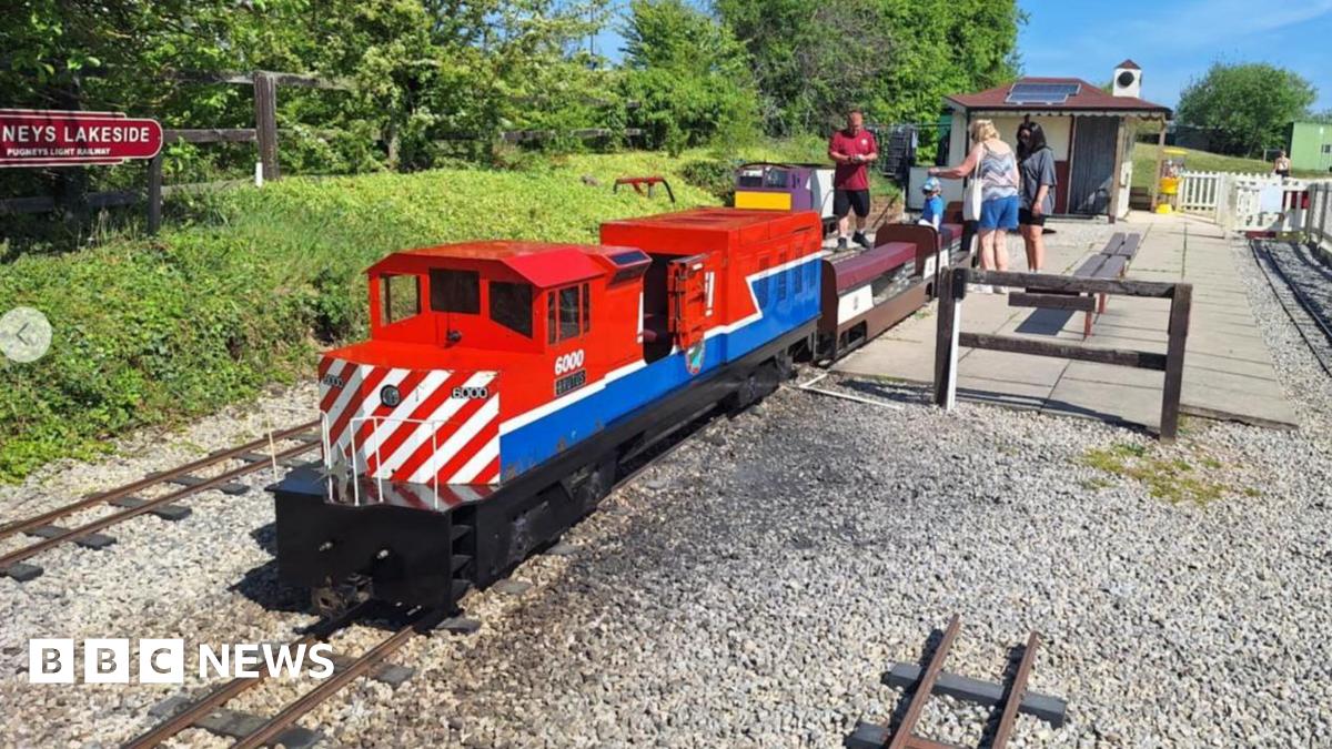 Man in blue suit stands beside a stone memorial to Sgt John Speed