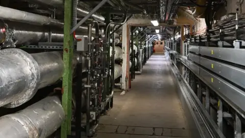 House of Commons A long corridor lined with large pipes and wires