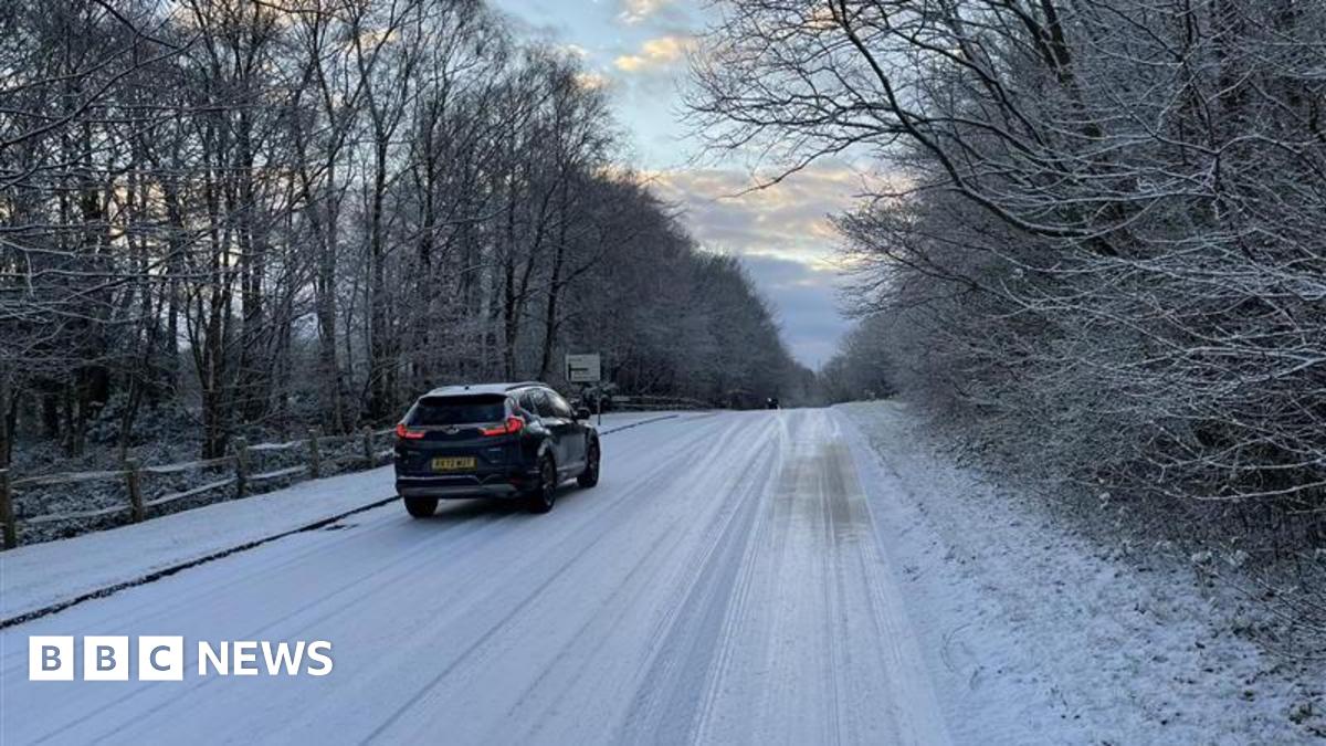 A car drives along a very snowy, entirely-white road