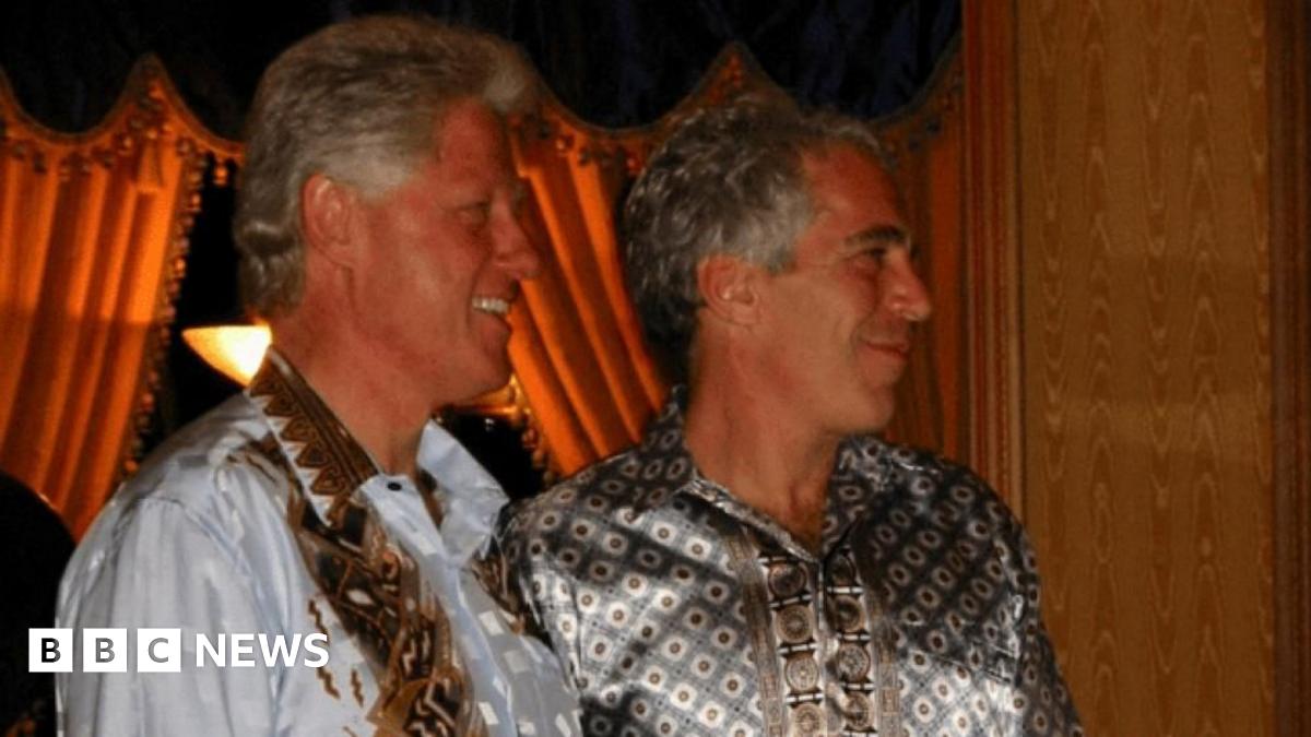 Former U.S. President Bill Clinton is standing next to Jeffrey Epstein and both men are wearing silky bron patterned shirts and smiling as they look to the right