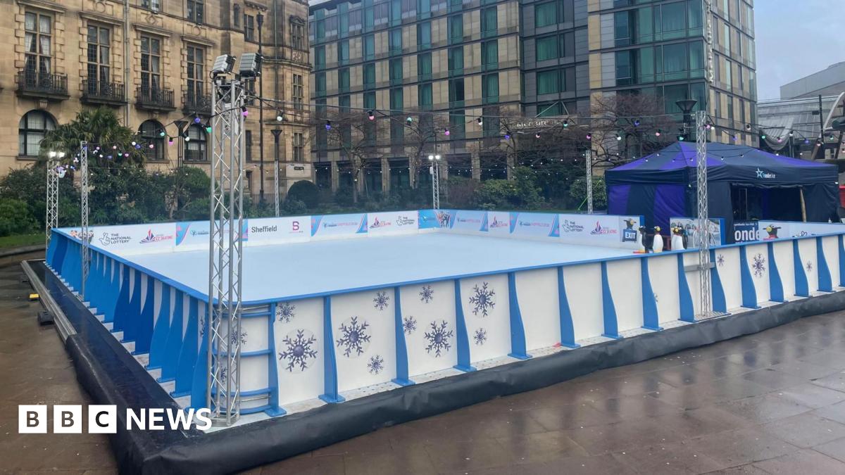 Millie Bobby Brown and David Harbour in character as Eleven and Jim Hopper. Eleven wears red shorts over grey leggings and a grey jumper. Jim Hopper wears a black leather jacket, a black beanie hat and dark trousers.They are speaking to director Frank Darabont on the set of Stranger Things. There is a vintage advertisement posted in the background with debrief on the ground.