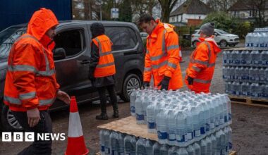 Four people in hi-vis orange jackets taking out bottled water supplies out of vehicles at a carpark.