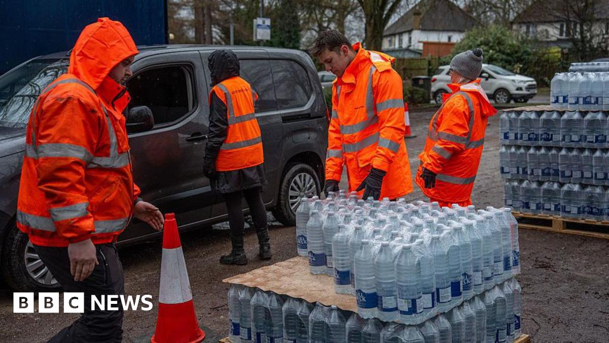 Four people in hi-vis orange jackets taking out bottled water supplies out of vehicles at a carpark.