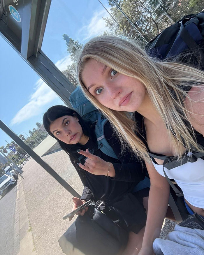 Two young women sitting at a bus stop, one holding a phone, relating to autopsy results in Canadian teen dingo case.