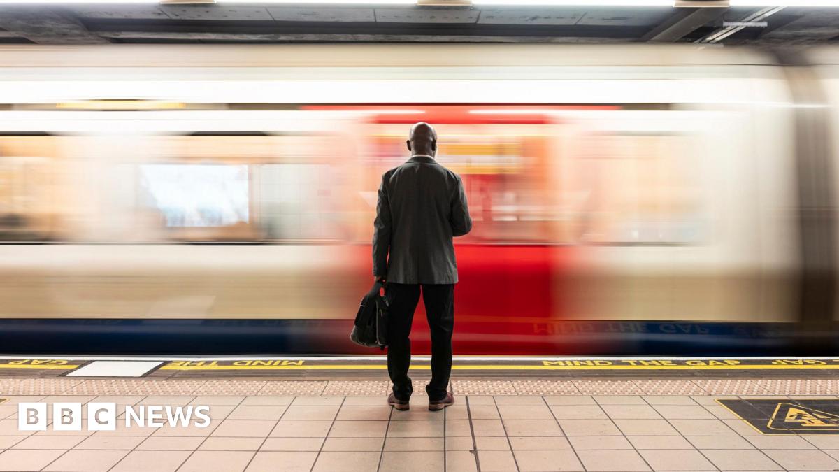 Senior passenger with laptop bag standing in front of speeding train on subway platform - stock photo