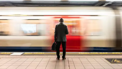 Getty Images Senior passenger with laptop bag standing in front of speeding train on subway platform - stock photo