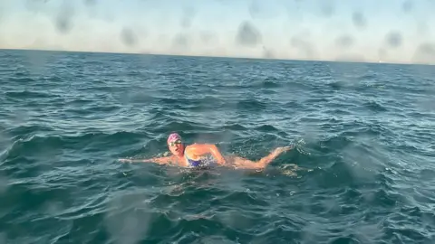 Victoria Rodwell Victoria Rodwell is swimming in the sea, doing front crawl. She is wearing a swimsuit, goggles and a swimming hat, and is turning on her side to breathe. the water is turquoise under a blue sky and there are drops of water on the camera lens.