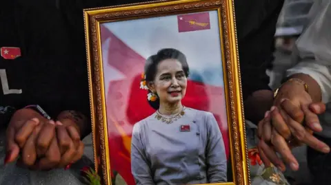 Getty Images A picture of detained civilian leader Aung San Suu Kyi is seen as Myanmar migrants living in Thailand hold hands during a memorial in Bangkok on March 4, 2021 to honour those who died during demonstrations against the military coup in their homeland.