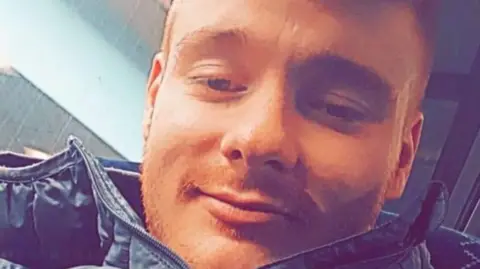 Spindrift Dylan Bennet, a man with red hair, a goatee and a moustache, smiles into the camera as he takes a selfie