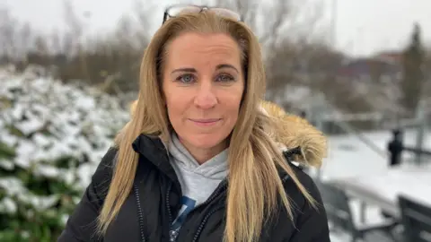 Blonde woman, Ms Knight. Close up photo taken in the snow outside. She wears a grey hoodie and a black fur-hooded coat.