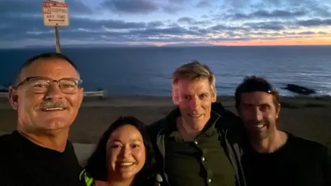 Chris Murray Three men and a woman are smiling while standing by the sea.