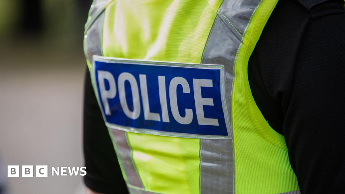 A close up of a police officer from the back wearing a black t shirt and high vis police vest