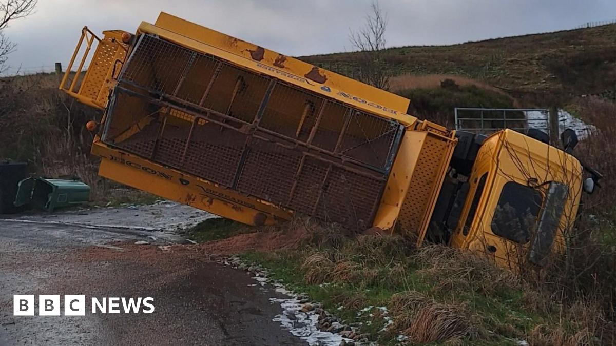 An overturned gritting lorry stuck in a ditch off a road on great, icy, wet moorland countryside