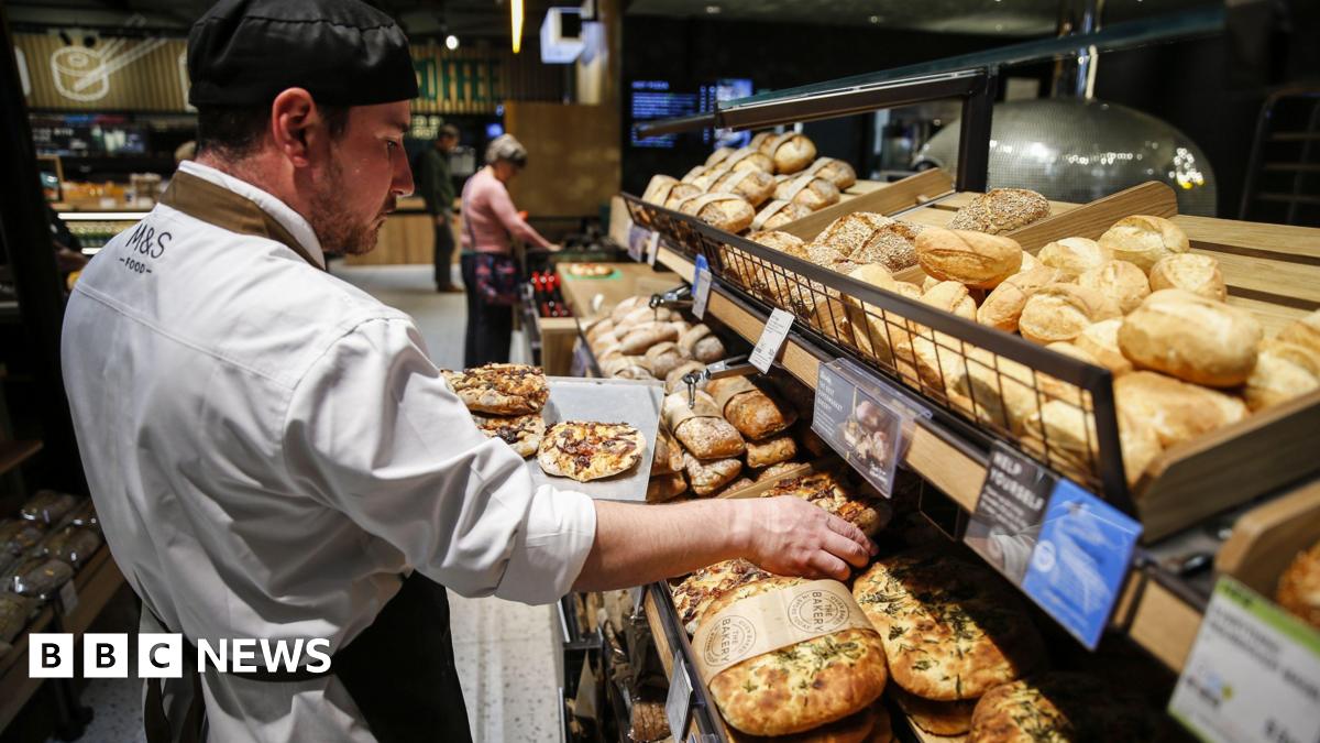 An M&S staff baker restocks the shelves full of pizza and bread rolls