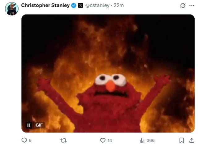 A screenshot of a post on X from Christopher Stanley of a well-known GIF of Elmo with hands raised in the air, and surrounded by fire.