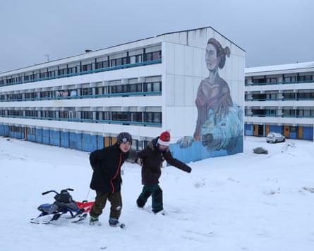 Children pull sleds through snow next to residential apartment buildings Nuuk, Greenland.