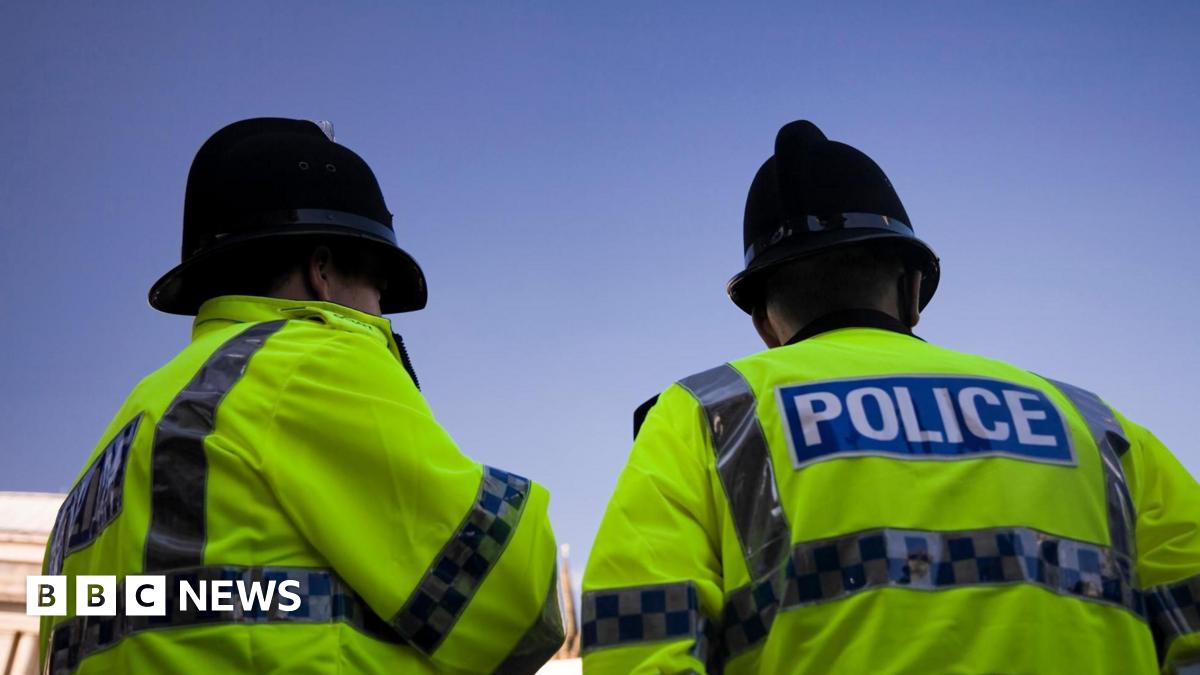 Two police officers stand together in fluorescent uniform and helmets looking out on a clear blue sky