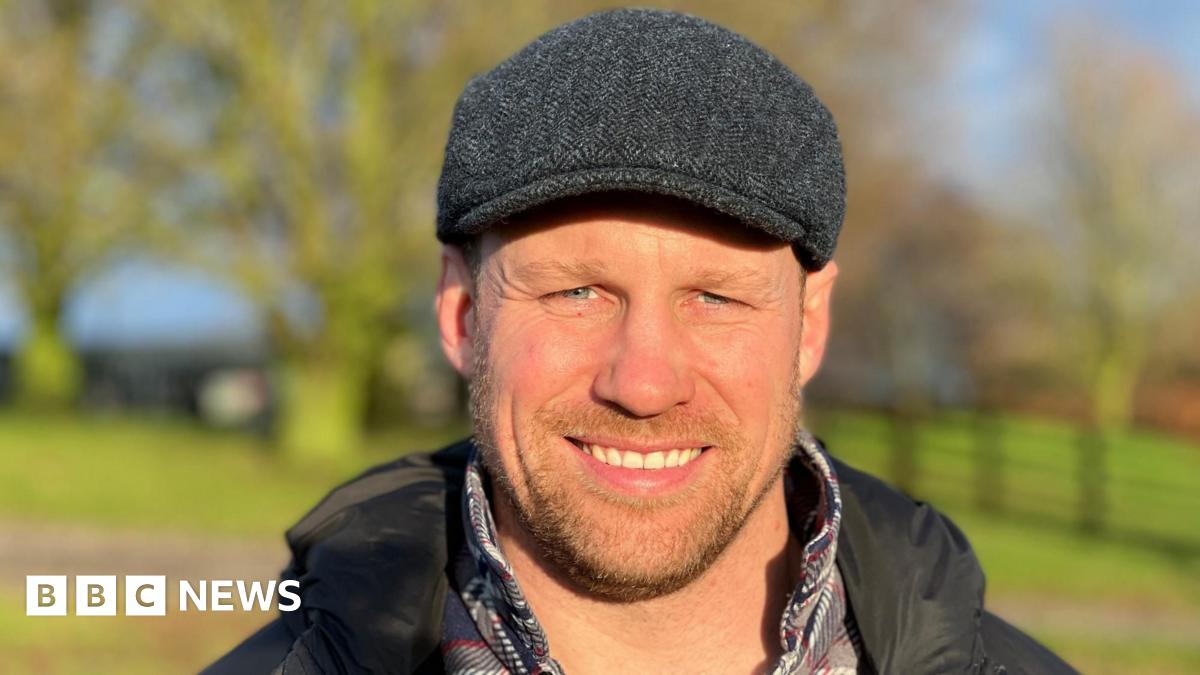 Farmer Oliver Collingham standing in a field of winter crops. The green vegetation stretches off into the distance as he looks across it.