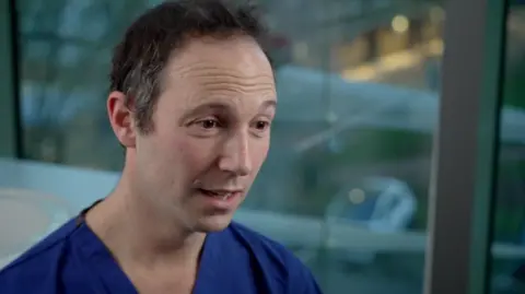 BBC News Mr Harry Petrushkin, who treated Nicki, is dressed in surgical scrubs and looks to the side of the camera