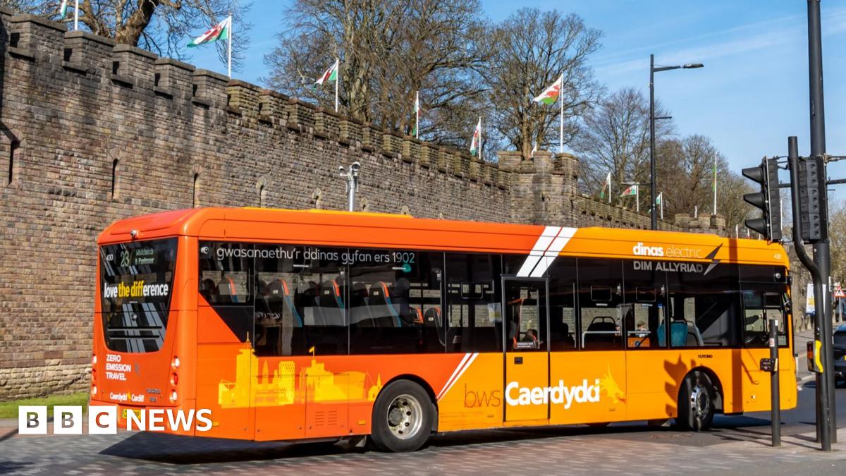 An orange single decker bus in traffic driving past Cardiff Castle.