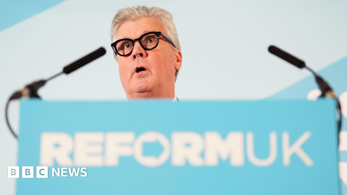 Malcolm Offord standing behind a podium with the Reform UK logo on it in white wirting on a blue background.