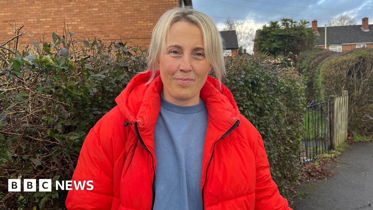 Millie Bobby Brown and David Harbour in character as Eleven and Jim Hopper. Eleven wears red shorts over grey leggings and a grey jumper. Jim Hopper wears a black leather jacket, a black beanie hat and dark trousers.They are speaking to director Frank Darabont on the set of Stranger Things. There is a vintage advertisement posted in the background with debrief on the ground.