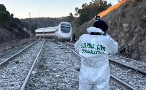 Spanish Guardia Civil / Handout via Reuters A person in white forensic overall saying 'Guardia Civil Criminalistica' hold a camera up to photograph the front of the train on the tracks.