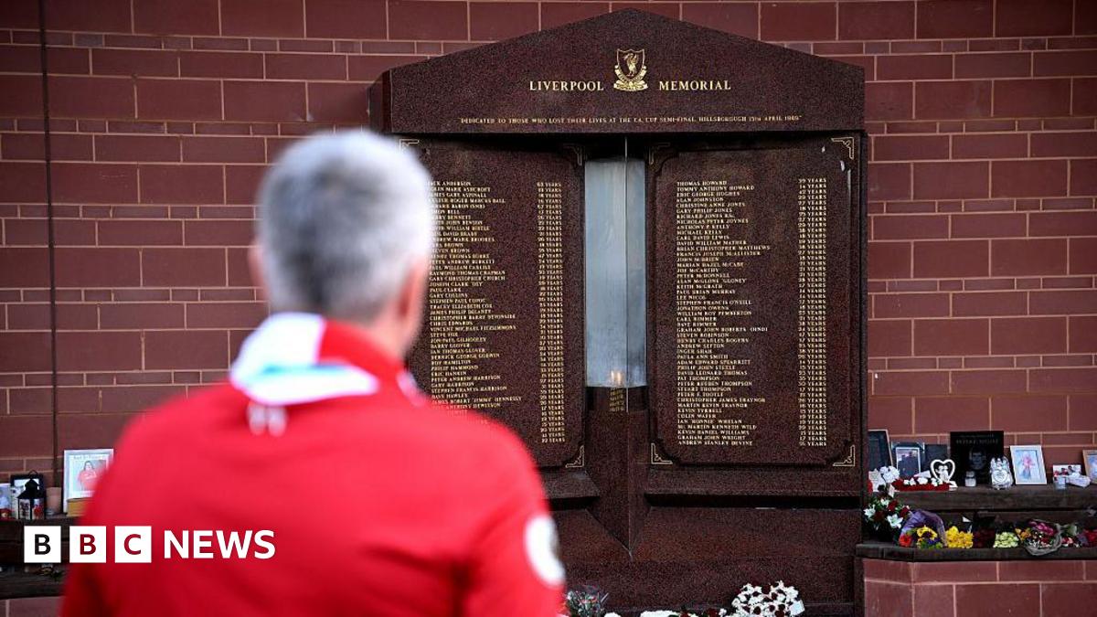 Millie Bobby Brown and David Harbour in character as Eleven and Jim Hopper. Eleven wears red shorts over grey leggings and a grey jumper. Jim Hopper wears a black leather jacket, a black beanie hat and dark trousers.They are speaking to director Frank Darabont on the set of Stranger Things. There is a vintage advertisement posted in the background with debrief on the ground.