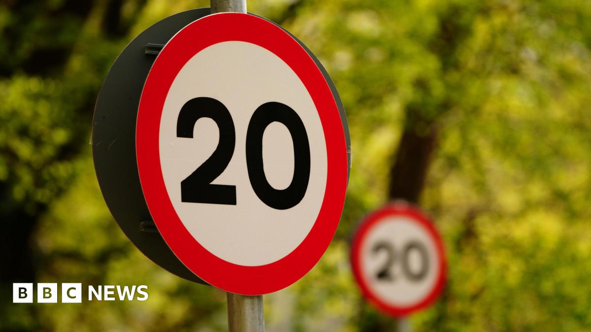 A big 20mph road sign with another in the distance, with trees in the background