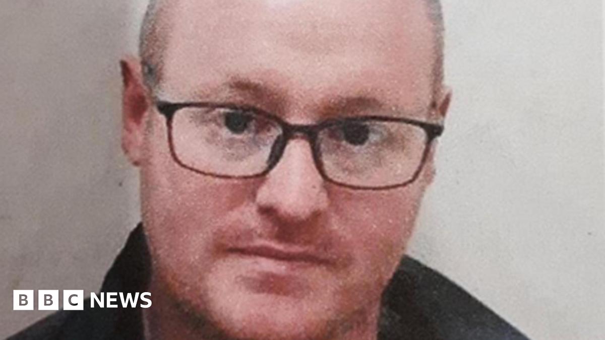 Matthew Armstrong is seen from his shoulders up in front of a white background. He is wearing black glasses.