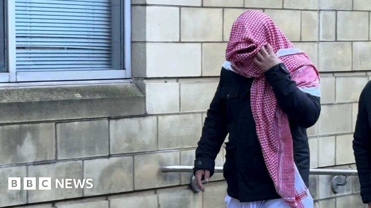 Ashraf Osmani, in a navy jumper with a red and white scarf obscuring his face, walks out of Northampton Crown Court.