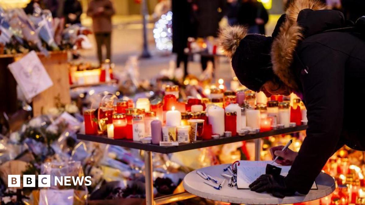 A woman signs a memorial book in front of floral tributes left outside to the victims of a fire at Swiss ski resort