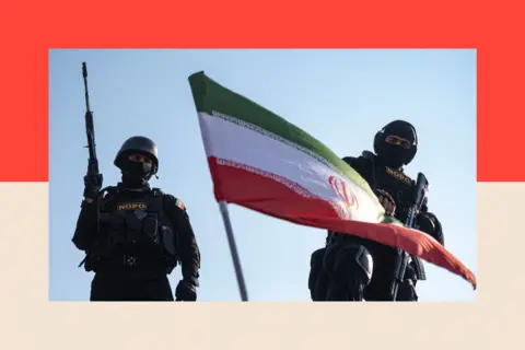 NurPhoto via Getty Images Two armed members of Iran's police special forces stand behind a country flag 
