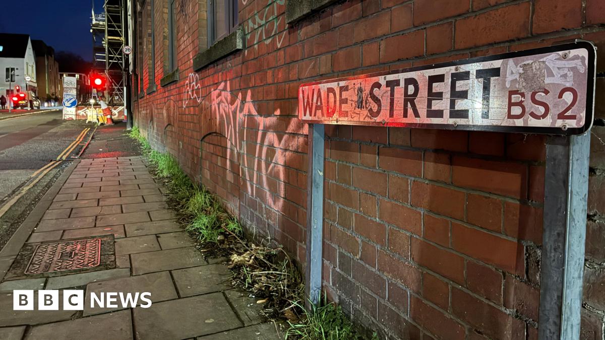 A view of Wade Street. with a street sign in the foreground and roadworks in the distance, there is graffiti on the redbrick wall.