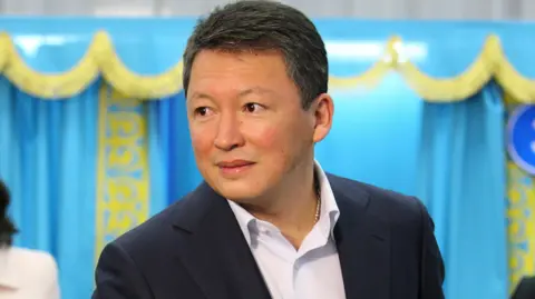 AP Photo/Nikita Bassov Timur Kulibayev, pictured in 2011 voting in Kazakhstan's elections. He is wearing a dark suit and a white shirt with no tie and has short dark hair. Behind him are curtains in blue with gold trim - the colours of Kazakhstan's flag.