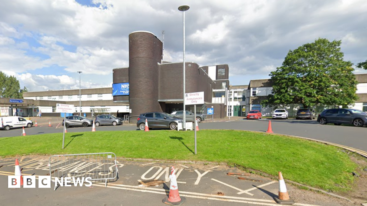 A large hospital building, with several vehicles parked in front