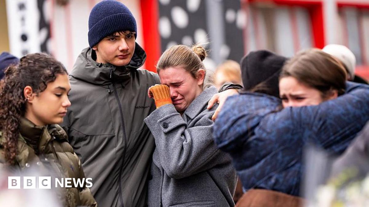 young people gather near the scene of a deadly bar fire. two groups of people can be seen hugging and crying.