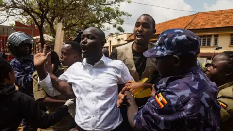 AFP via Getty Images A man in a shirt holds his arm up and exclaims while being restrained by people in uniform