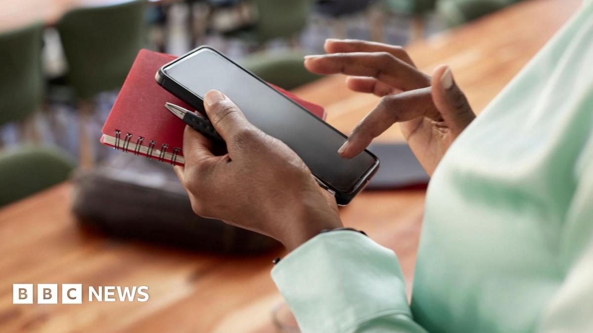 Woman types on phone while holding a notebook and a pen