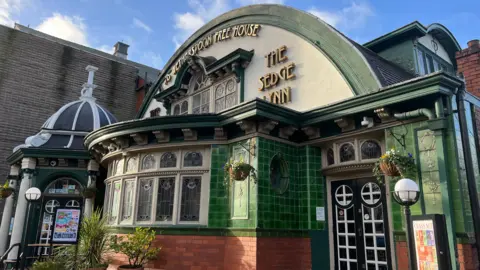 BBC A view of the Sedge Lynn pub. It shows the frontage with distinctive green tiles and a domed roof.