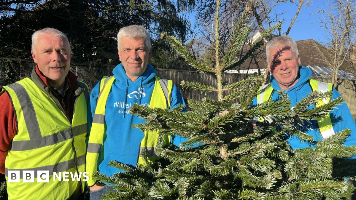 Dave, Ian and Pete Ruffett smile at the camera as they are photographed outside holding a Christmas tree. They are all wearing high-visibility jackets and hoodies underneath.