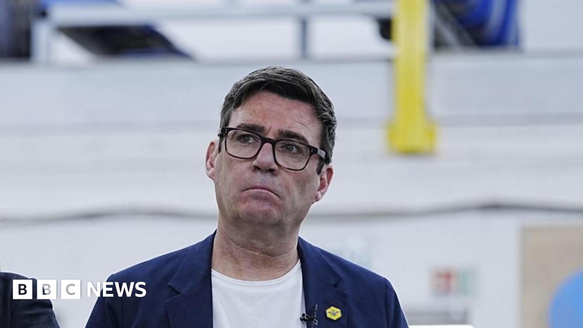 Headshot of Burnham who looks up and to the right. He has a serious expression. The background is blurry.