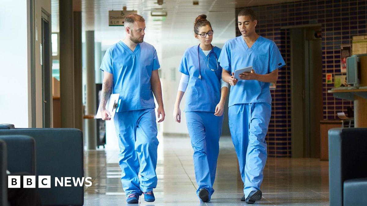 Three junior doctors walking down a hospital corridor while wearing blue scrubs