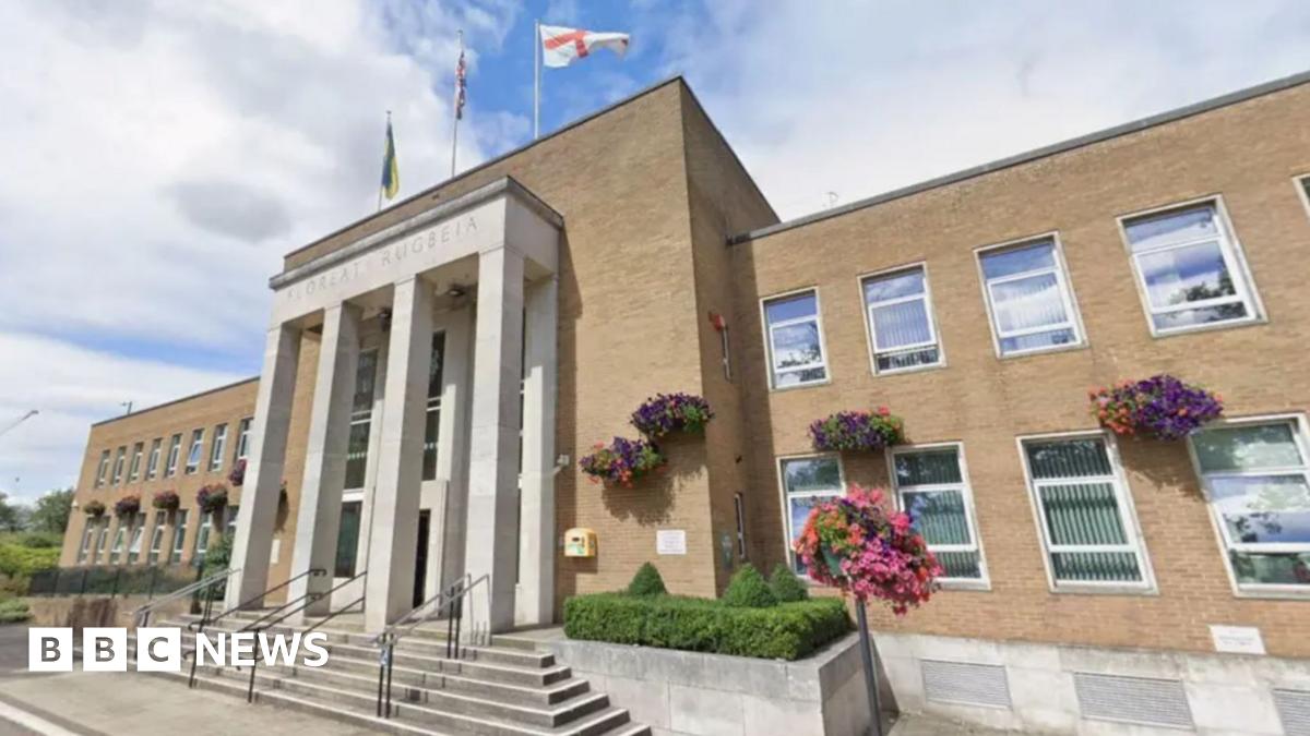 The front of a large light-brown building with white pillars surrounding an entranceway