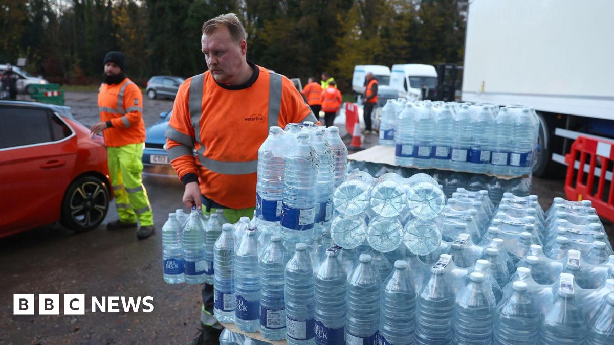 People in orange high-vis tops moving pallets of bottled water around a muddy car park