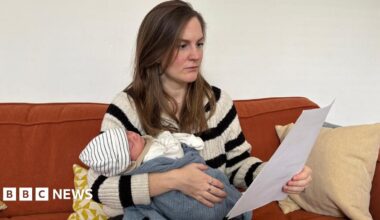 Beth Kojder holding her newborn baby and reading through an energy bill