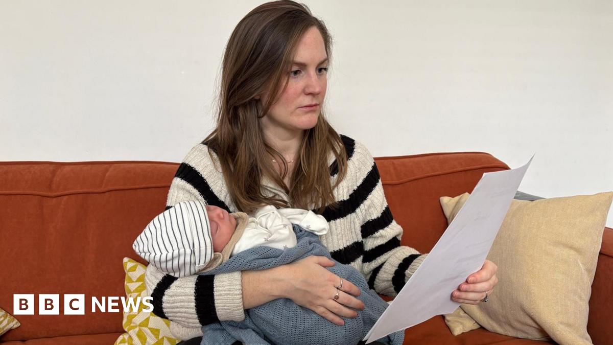 Beth Kojder holding her newborn baby and reading through an energy bill